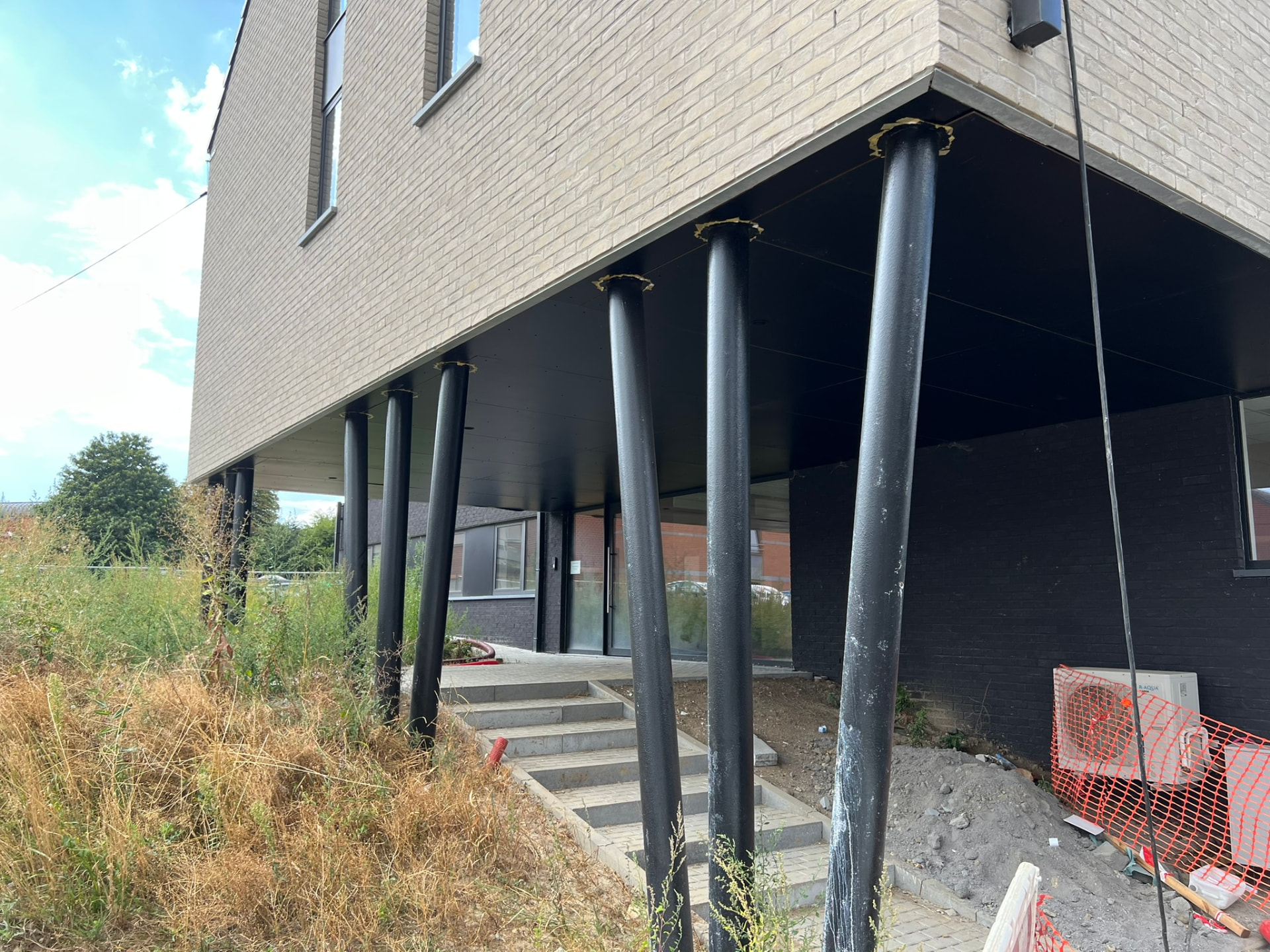 Colonnes métalliques noires portant le volume en porte-à-faux au-dessus de l'entrée