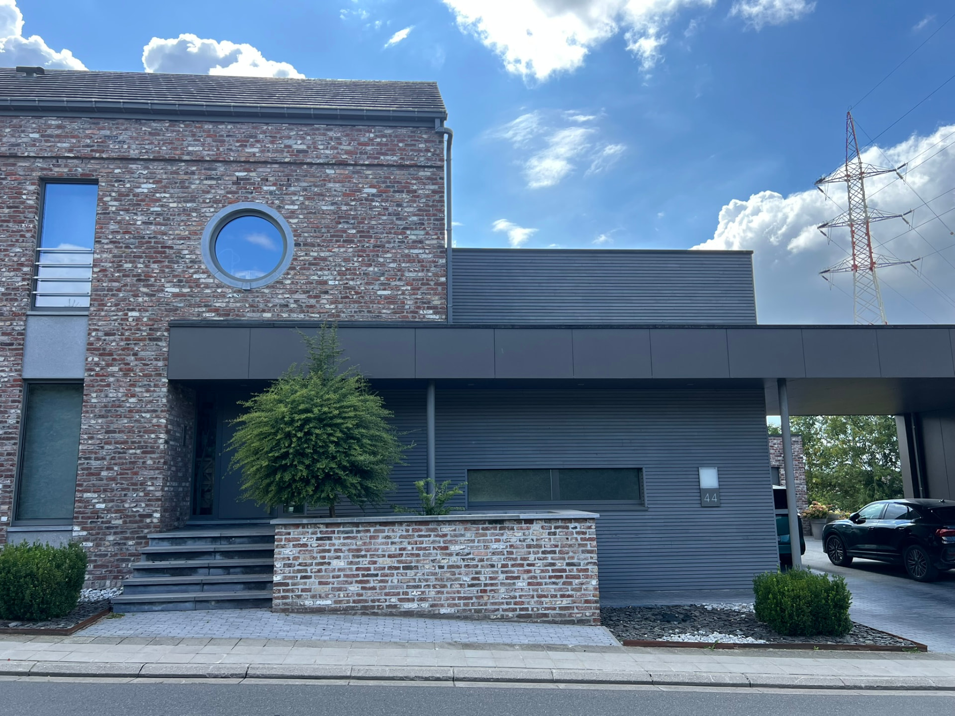 Façade d'entrée avec perron en pierre bleue, muret en briques et auvent sombre