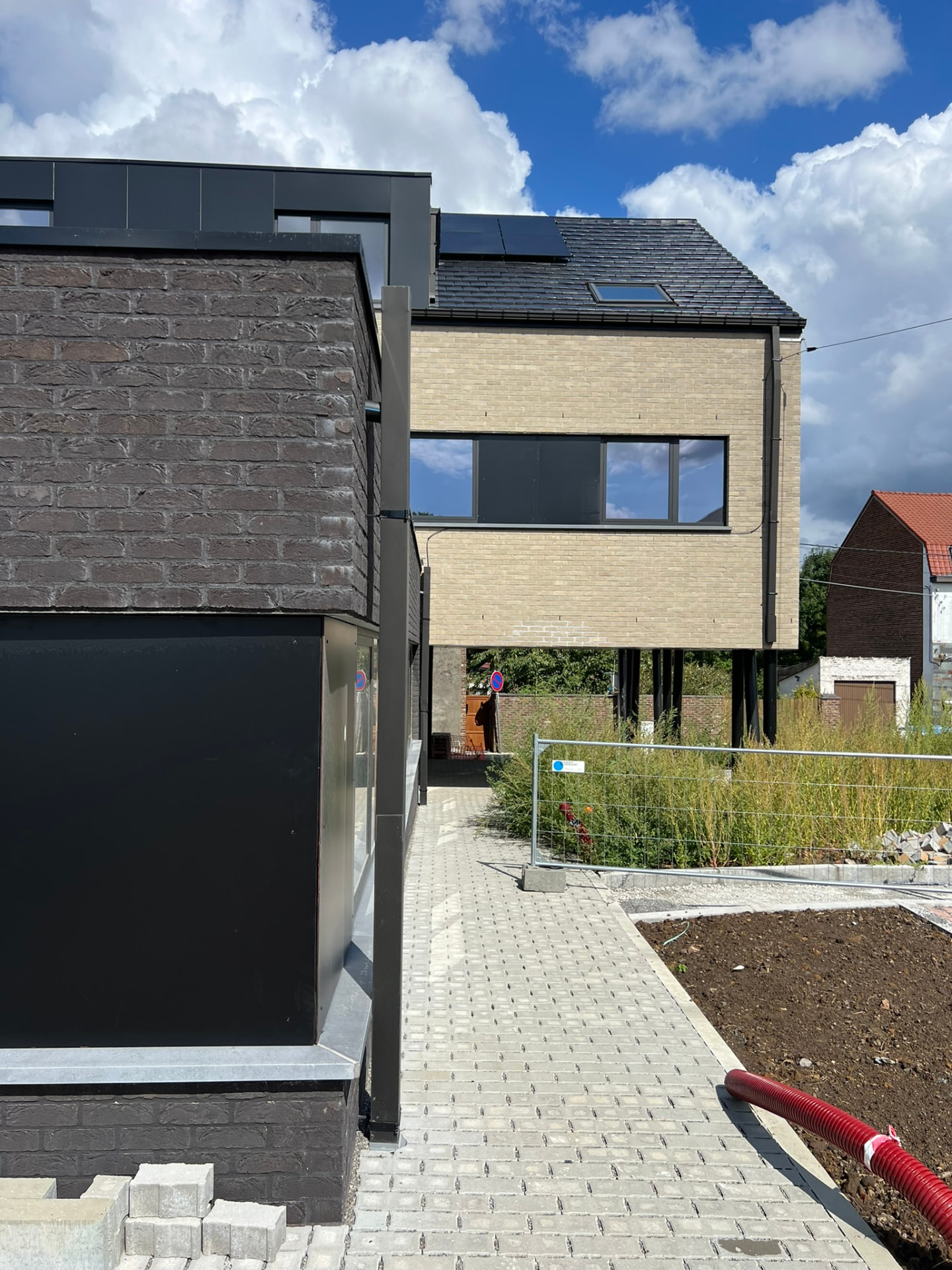 Cheminement pavé entre l'annexe basse en briques sombres et le volume sur pilotis