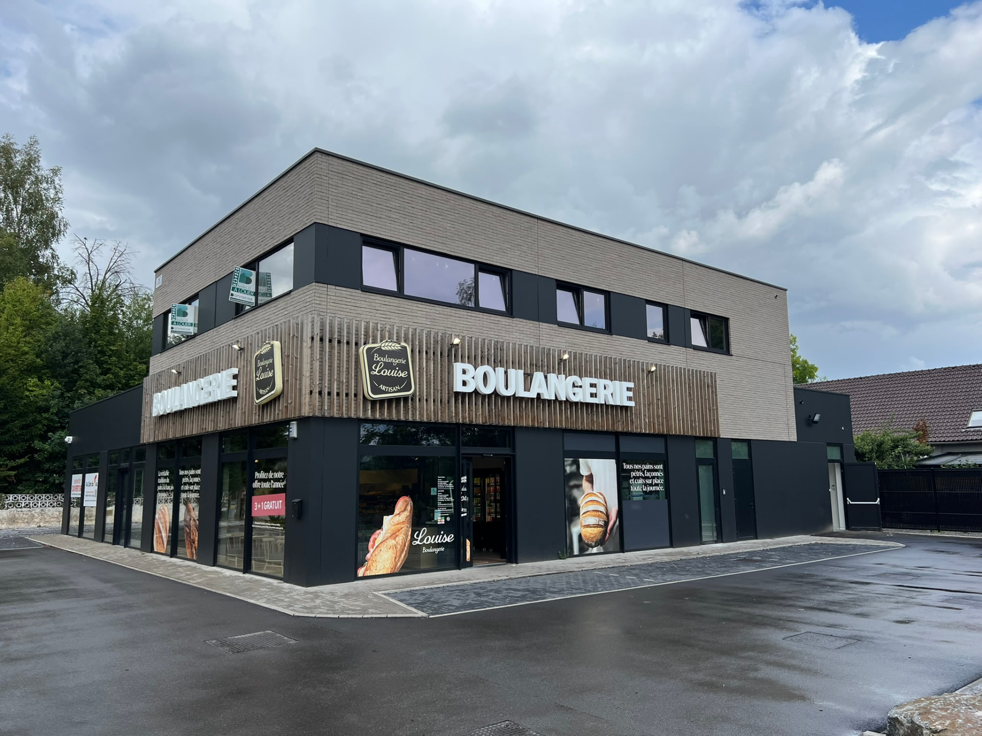 Vue d'angle du volume commercial : soubassement vitré sombre et étage en briques claires