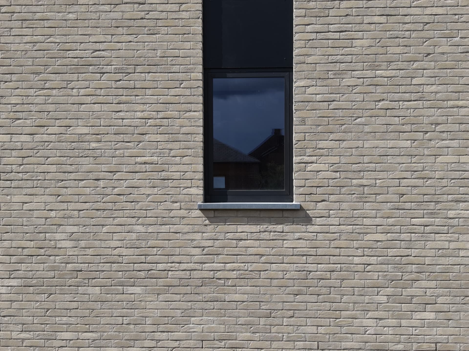 Détail d'une fenêtre verticale en menuiserie noire dans la façade en briques claires