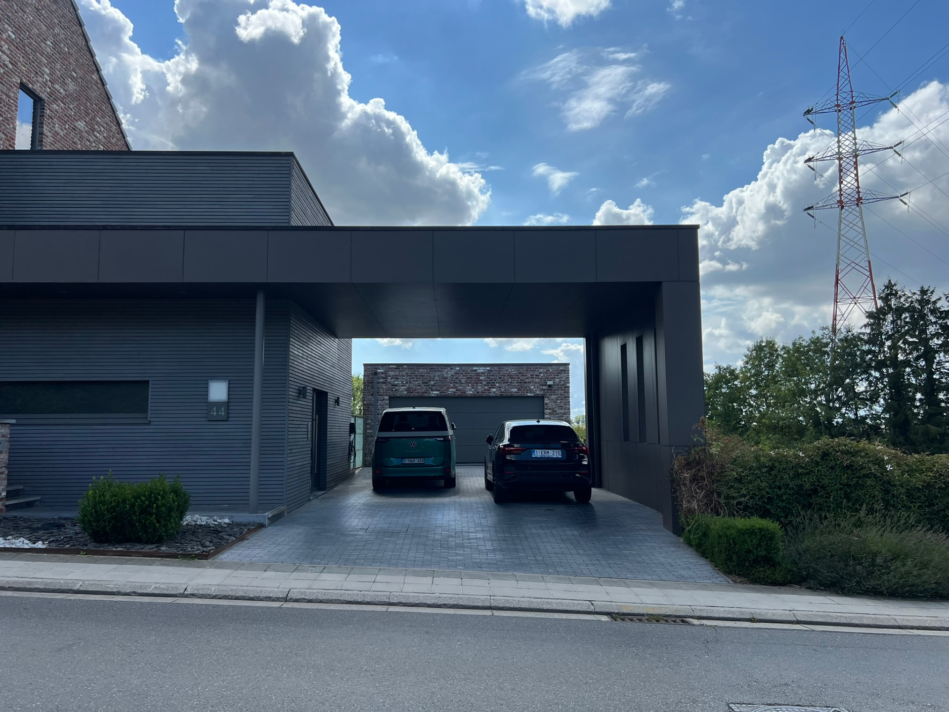 Carport ouvert sur le jardin, entre le volume bardé et le mur en briques du garage