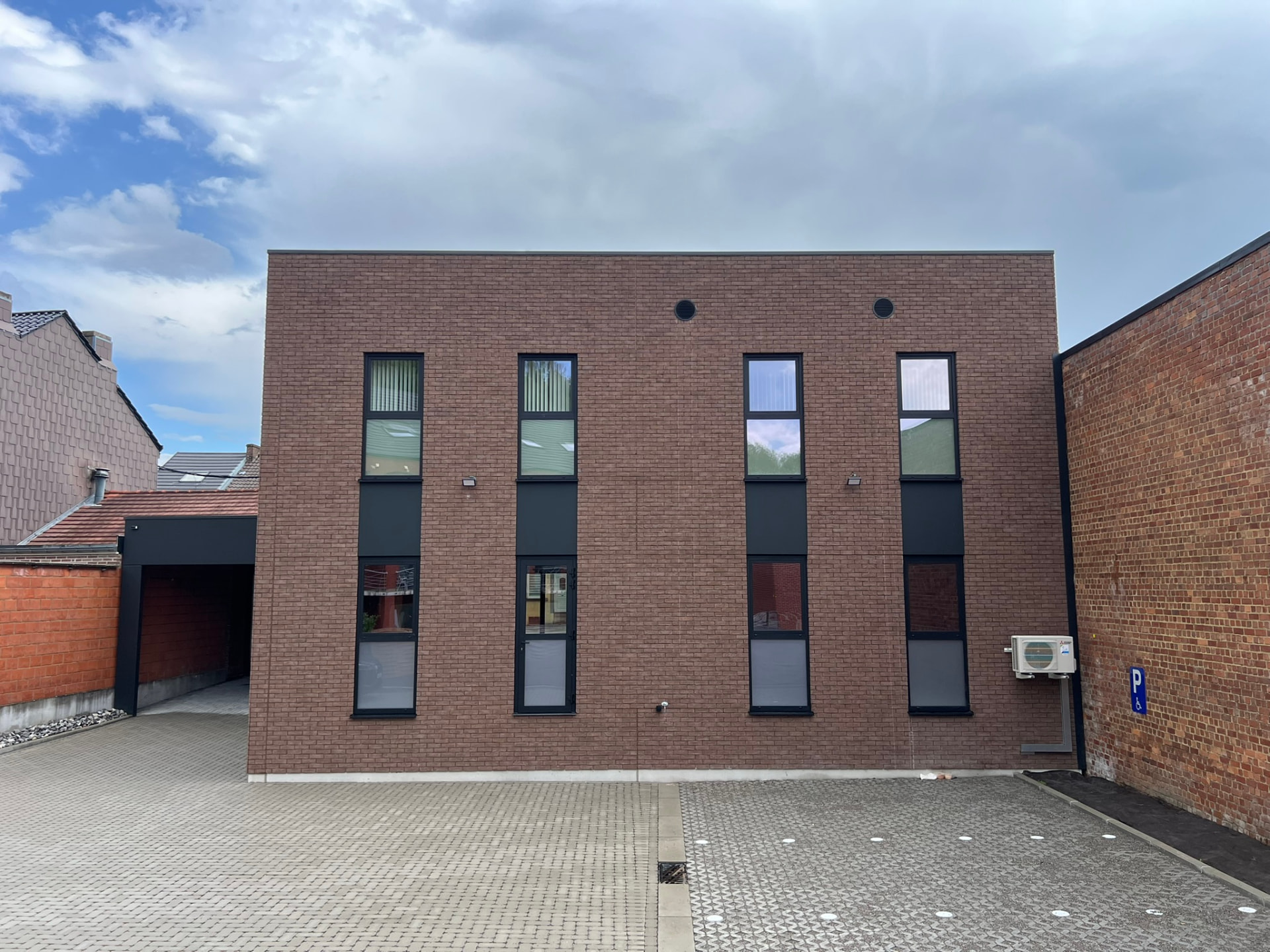 Façade arrière en briques avec fenêtres verticales et parking pavé