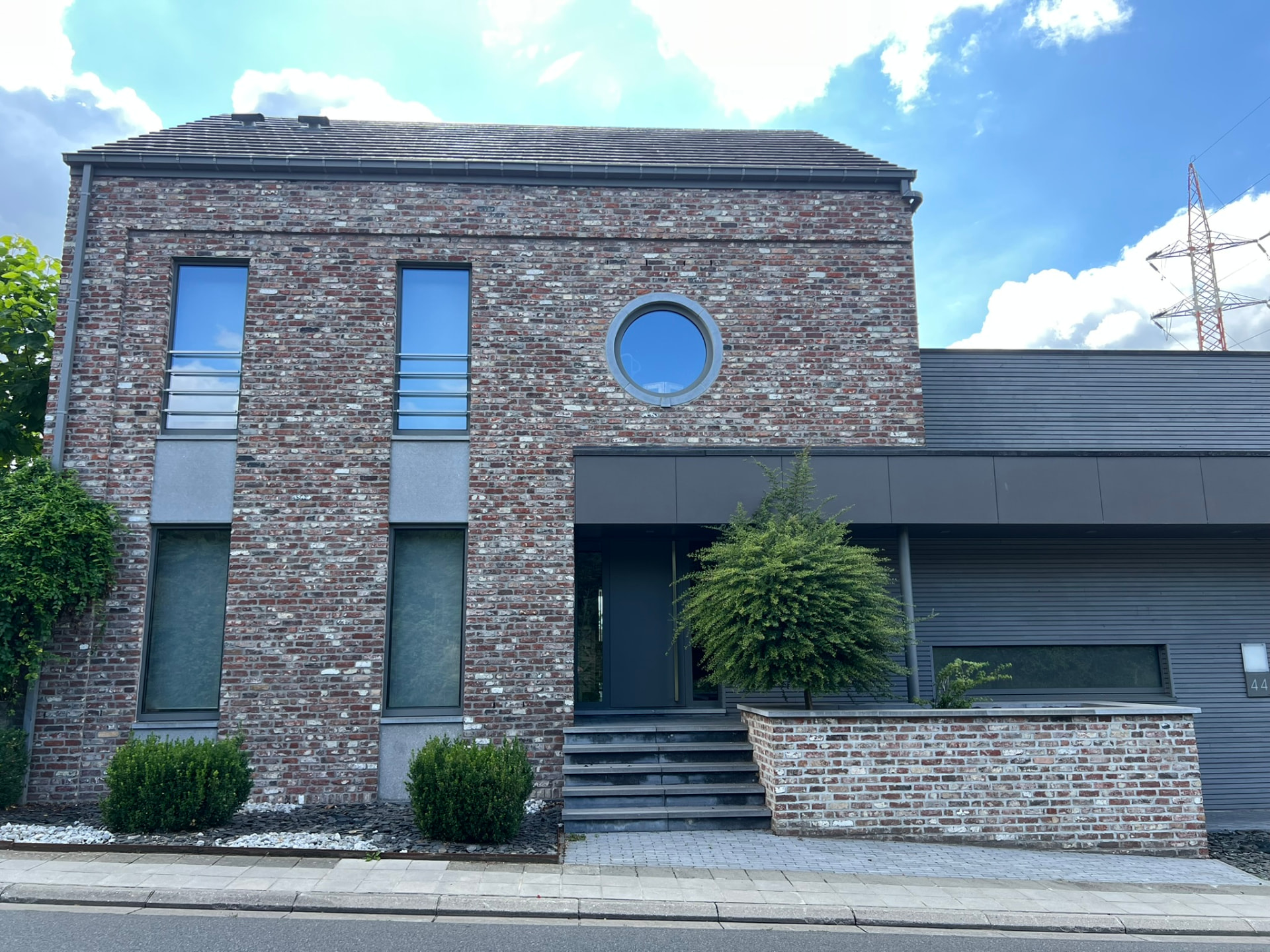 Façade rue d'une habitation contemporaine en briques de récupération percée d'un oculus