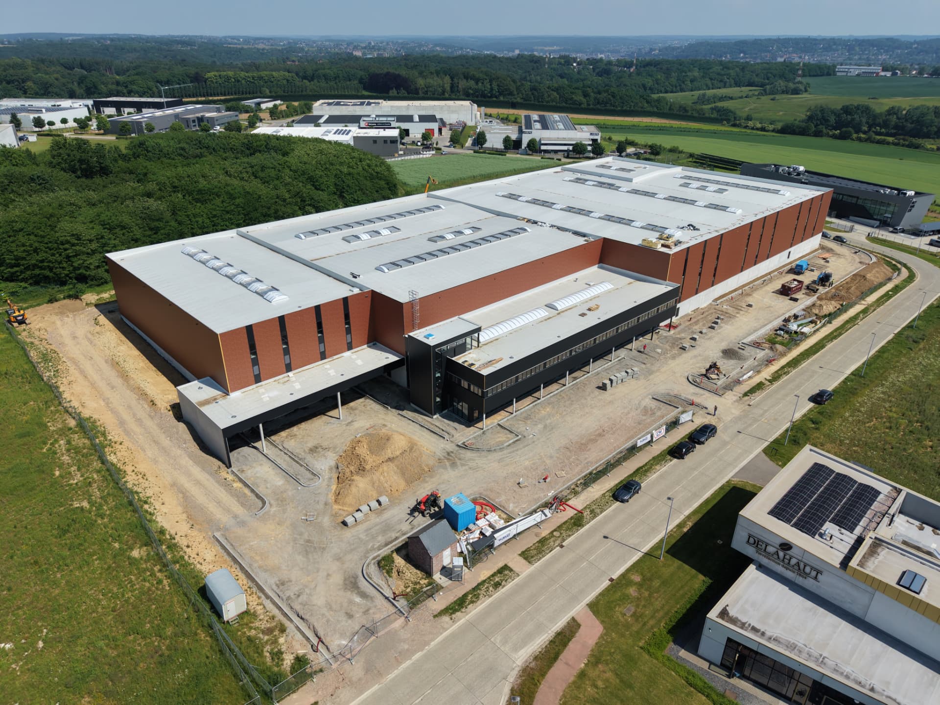 Vue aérienne d'un vaste bâtiment industriel à bardage terracotta et toiture claire en cours d'achèvement