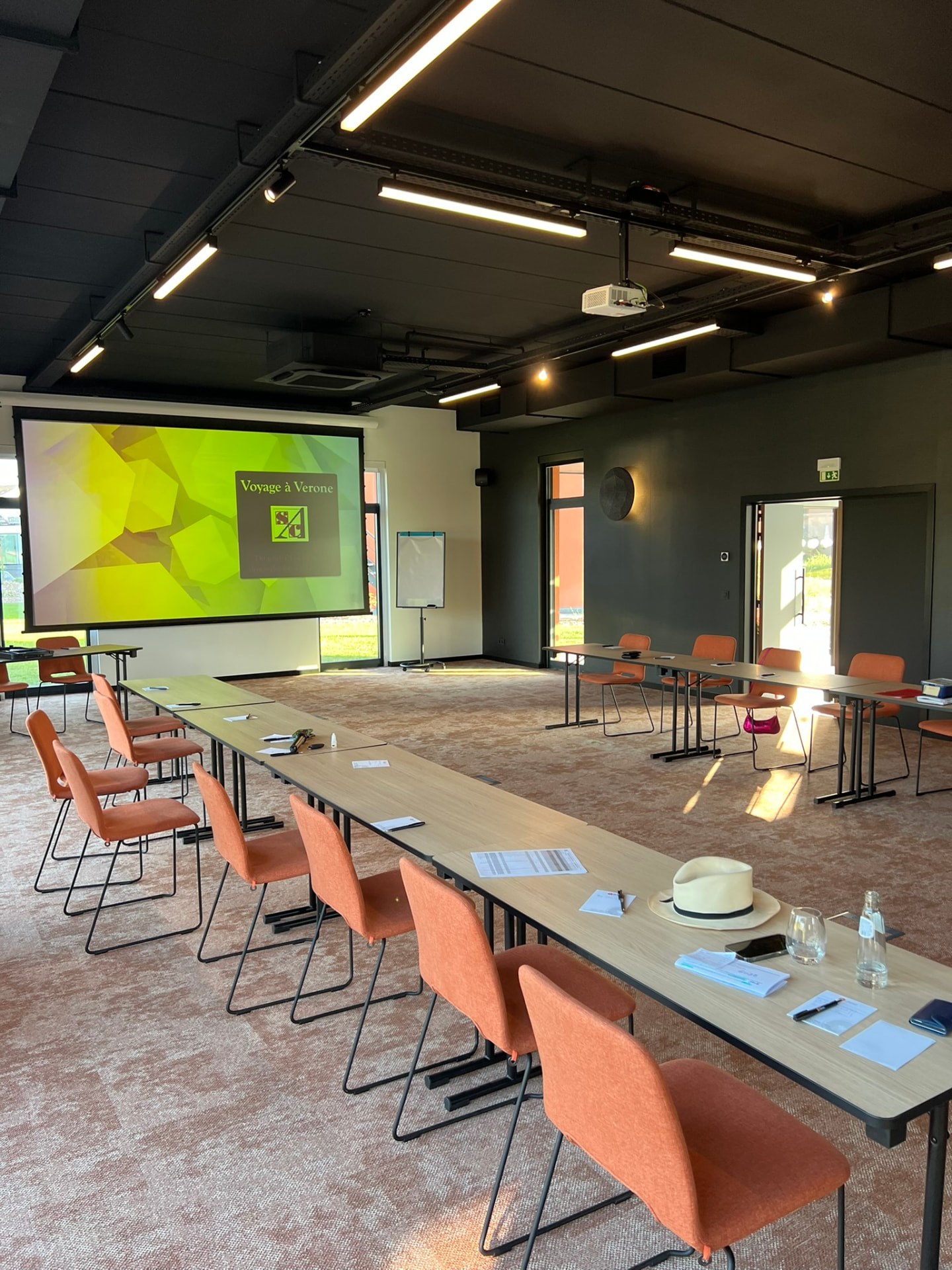 Salle de séminaire avec plafond technique noir, écran de projection et mobilier terracotta