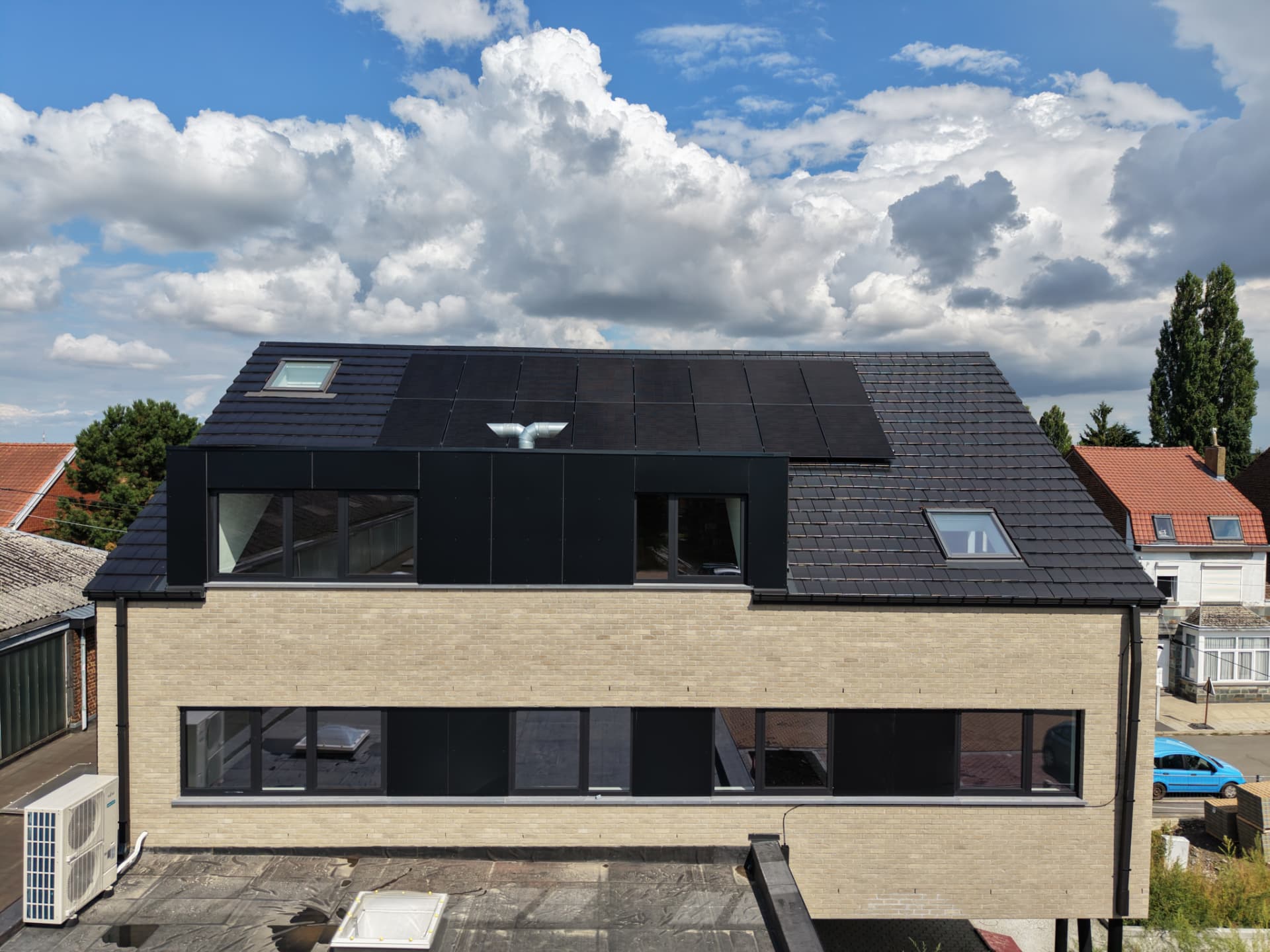 Toiture en tuiles noires avec panneaux photovoltaïques et lucarne en bardage sombre