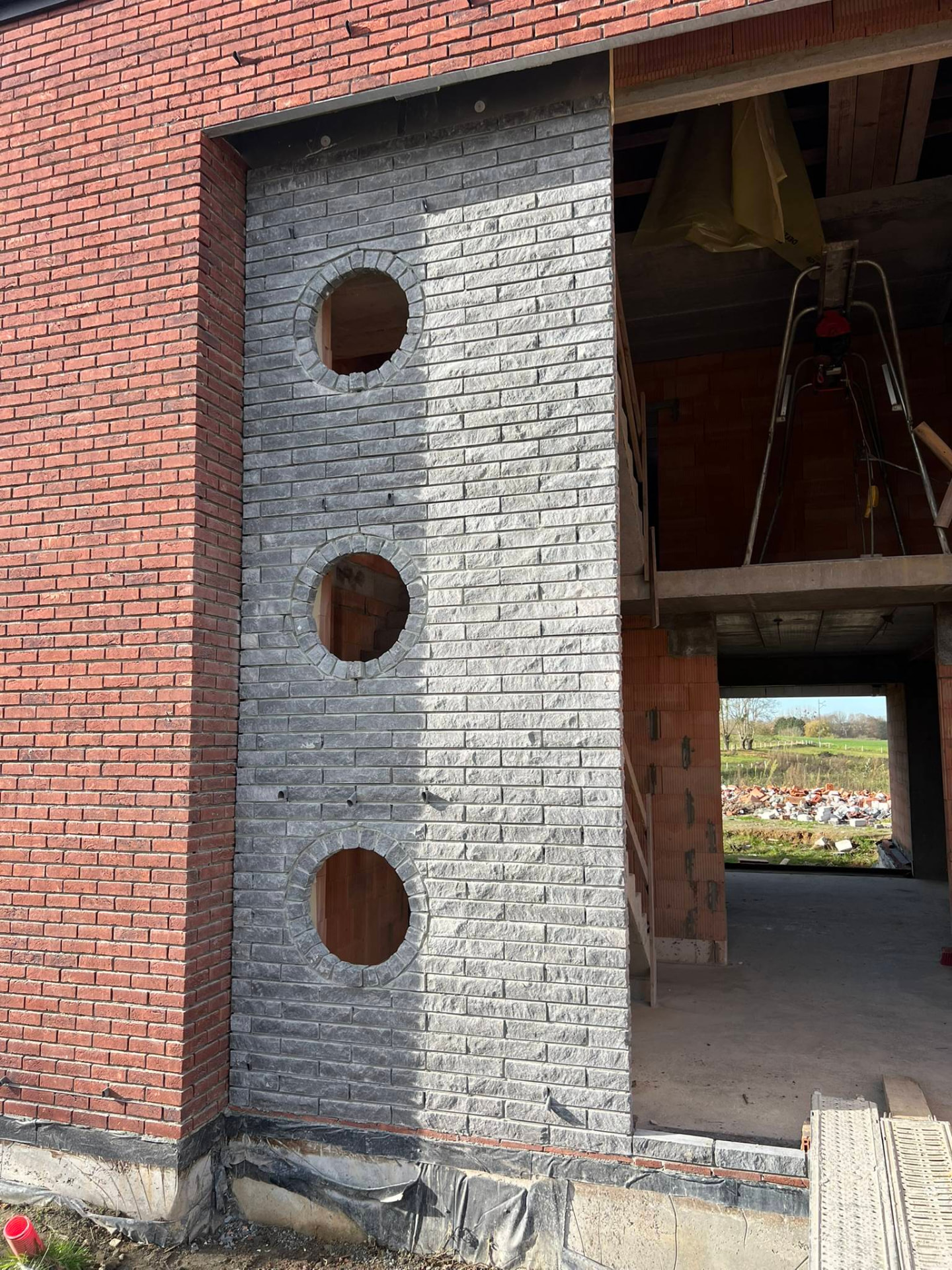 Détail de chantier du parement en briques grises percé de trois oculi