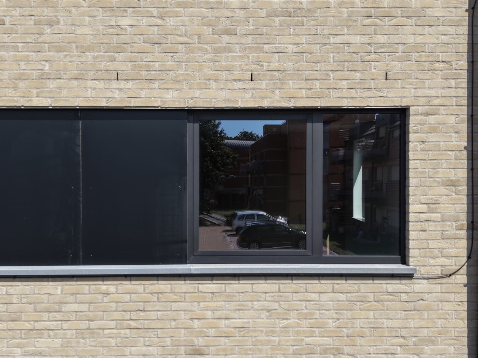 Détail d'une baie horizontale en menuiserie noire dans la façade en briques claires
