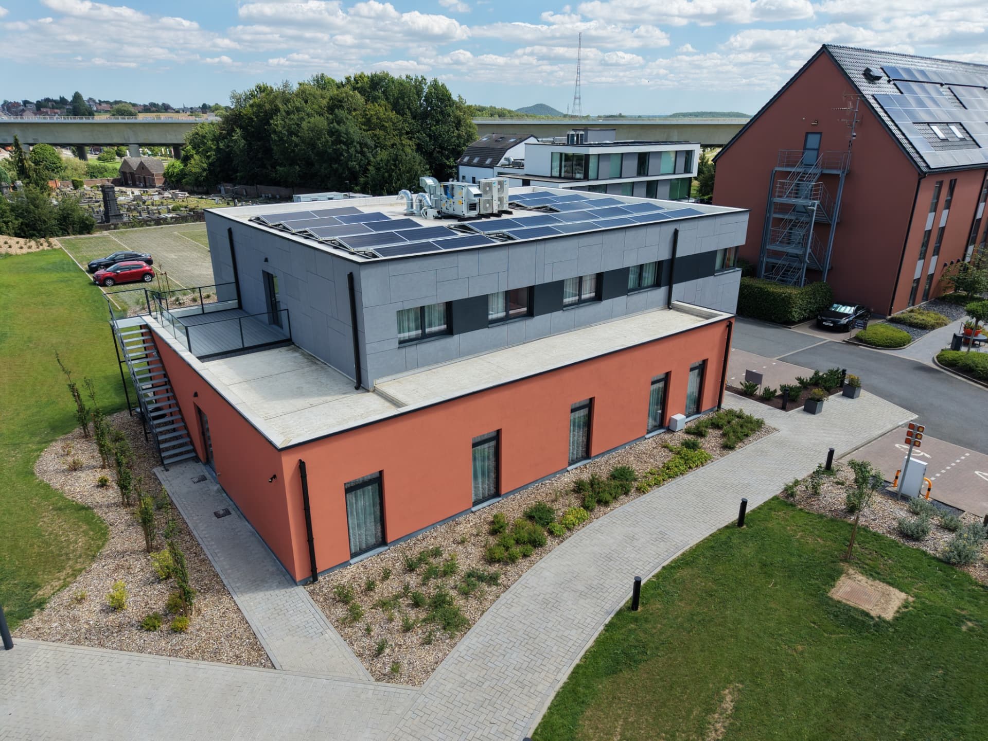 Vue rapprochée du bâtiment d'accueil avec terrasse, escalier extérieur et panneaux solaires en toiture