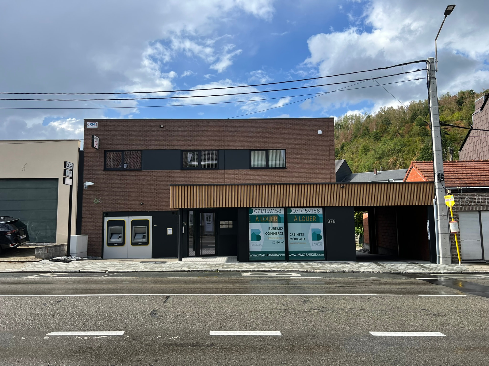 Façade principale du bâtiment en briques brunes avec auvent en bois et vitrines commerciales
